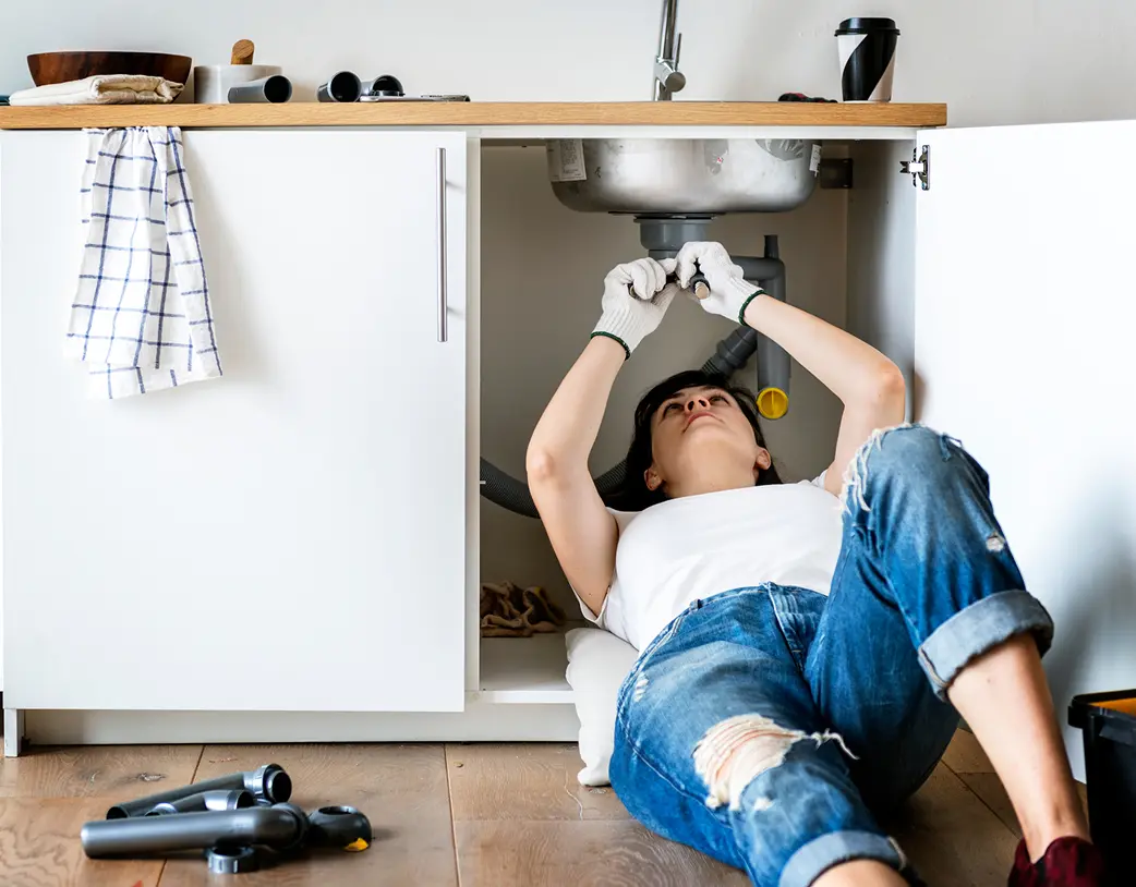 Woman laying down in sink working on plumbing above her