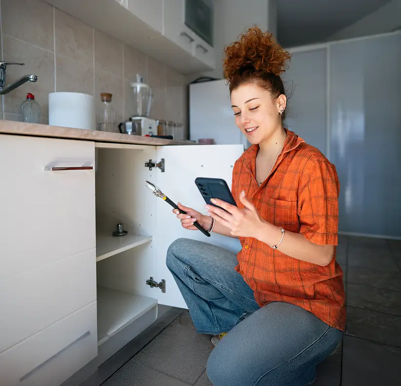 Woman kneeling down watching tutorial before working on sink.